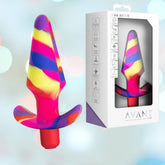 The Avant Free Spirit Vibrating Anal Plug - Scarlet is a colorful silicone plug with an abstract pattern of red, yellow, blue, and pink swirls. It features a flared base for safety and offers 10 vibrating functions. Its white box packaging, labeled "Avant," showcases the waterproof vibrating anal plug through a transparent window.